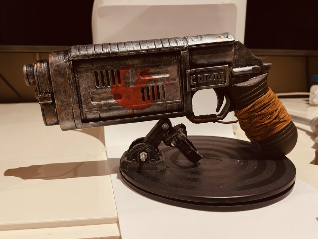 Weathered handmade sci-fi blaster displayed on a stand